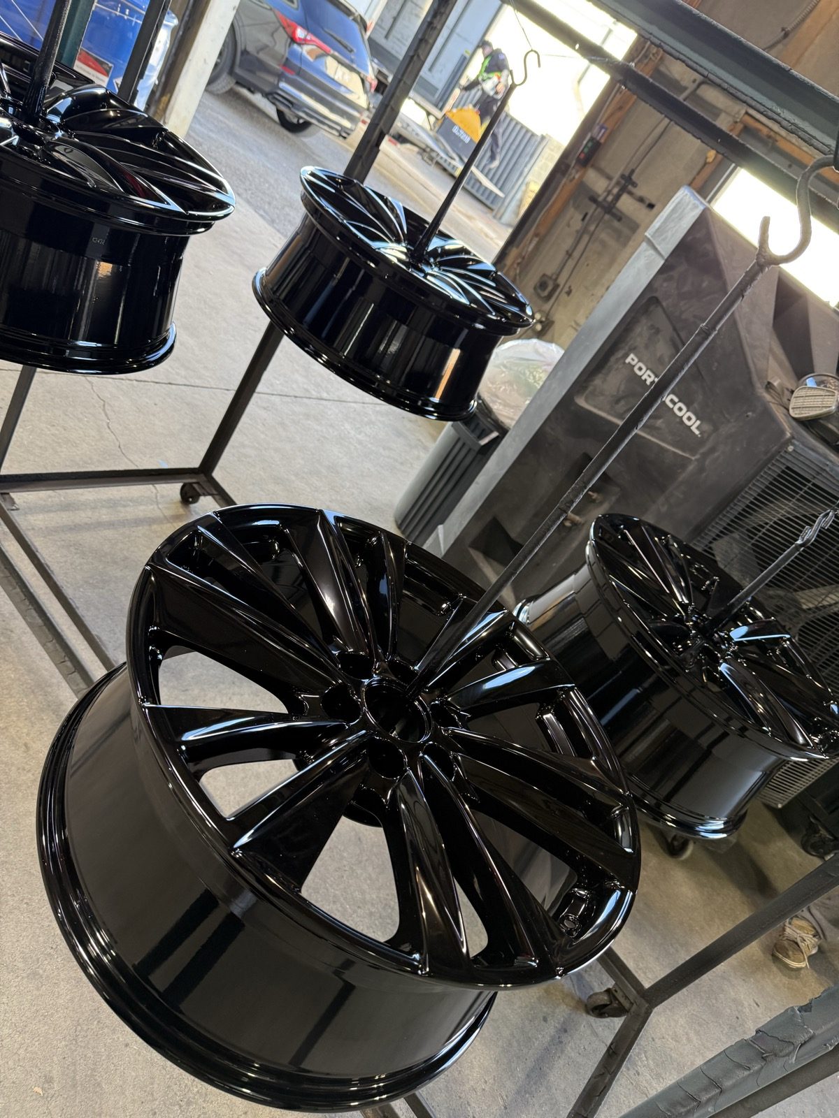 Several gloss black wheels hanging on the rack after curing