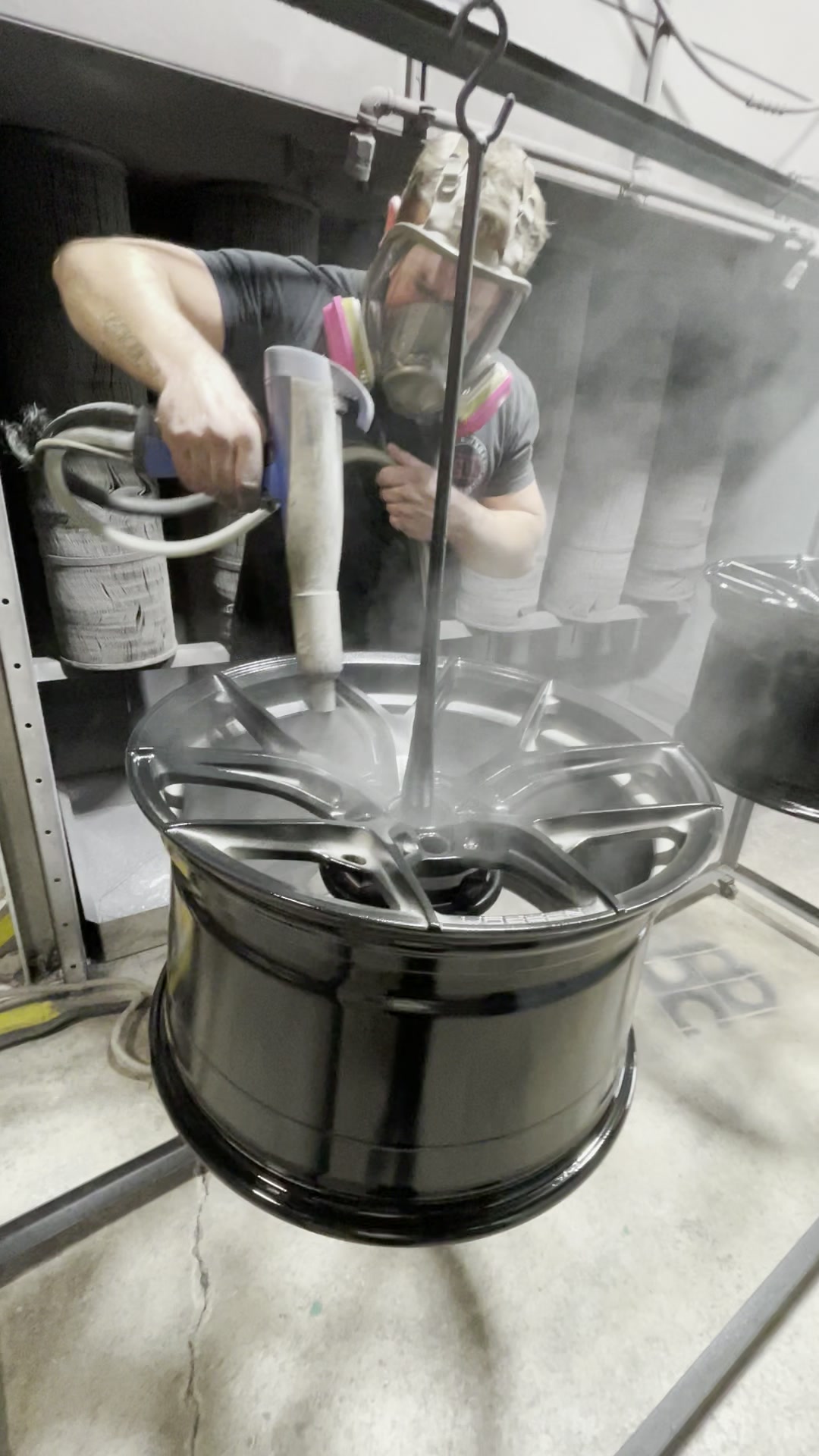 Technician applying gloss black powder to a multi-spoke wheel in the ColorWerks spray booth