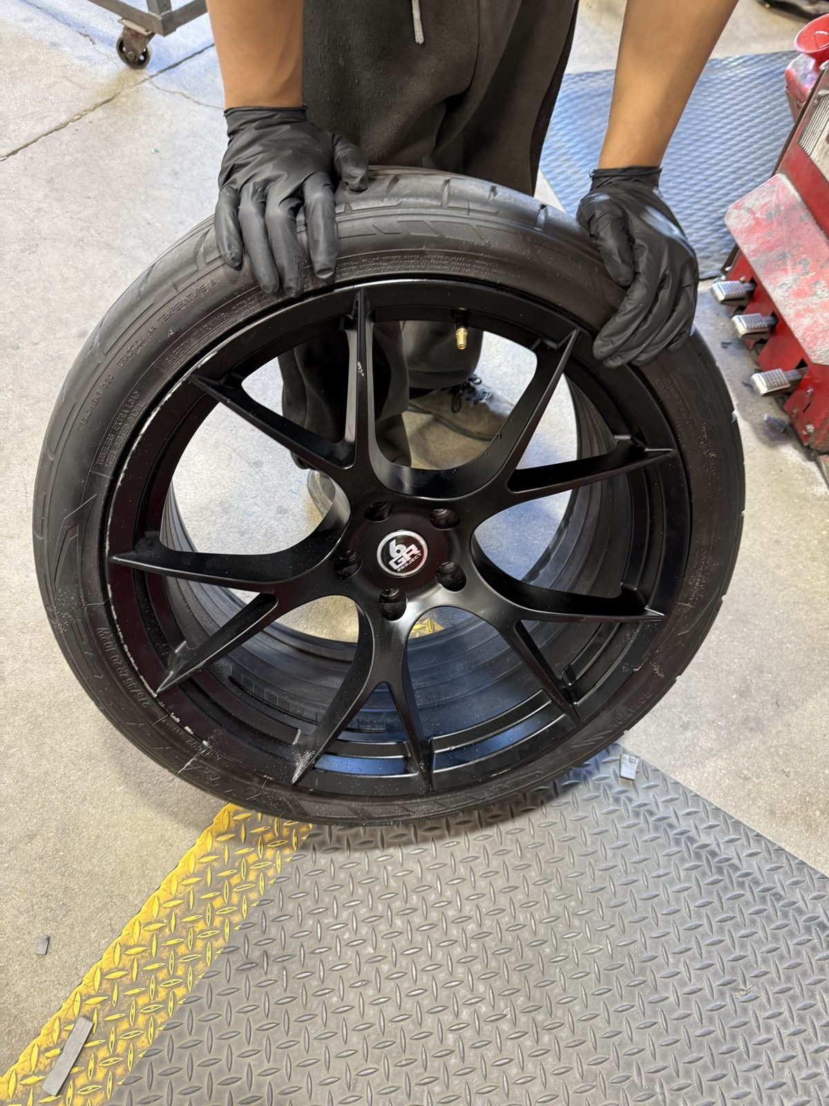 Technician remounting a tire on a freshly powder coated gloss black wheel — mount and balance are included