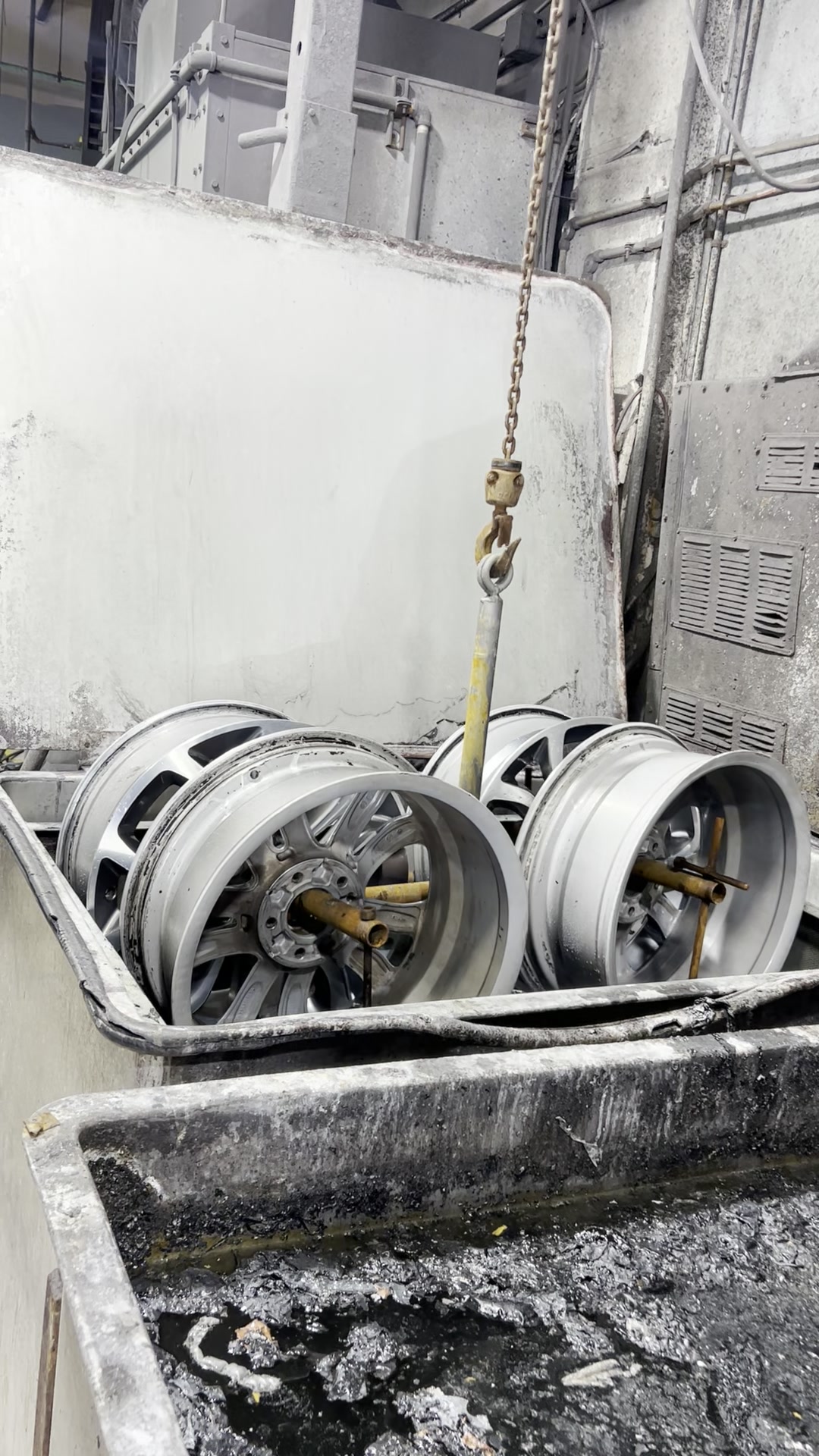 Alloy wheels on a chain going into the strip tank at ColorWerks — old finish removed chemically, no media blasting