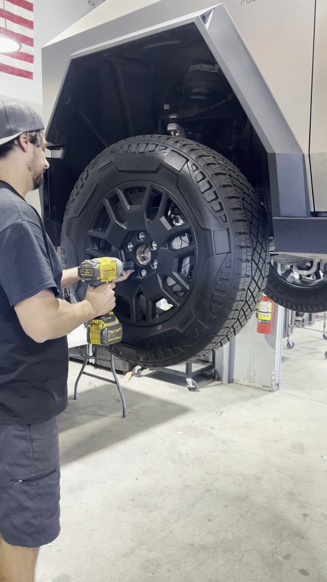 Technician installing a black powder coated wheel on a lifted Tesla Cybertruck